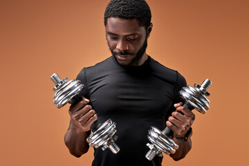 Fototapeta na wymiar african male concentrated on exercises with dumbbells, looking at them, weightlifting