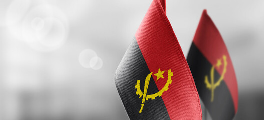 Small national flags of the Angola on a light blurry background