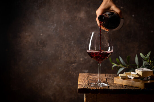 Pouring red wine into the glass against rustic dark wooden background