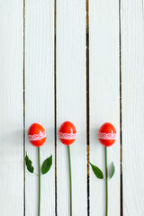 Three red eggs aranged as flowers with on white wooden background. Creative Easter concept. Flat lay.