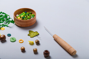 Close up of awl, box of beads and buttons, tape or ribbon for sewing and embroidery. Green and yellow set of materials for handcraft, making of bijouterie and accessories. Copy space.