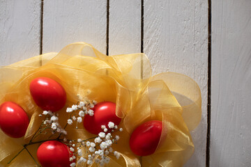 Red easter eggs decorative aranged with yelow ribbon as nest and whit tine flowers on wooden table.