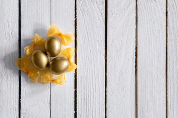 Golden color eggs decorative aranged with yellow bow on white wooden background. Minimal Easter concept and idea. Flat Lay.