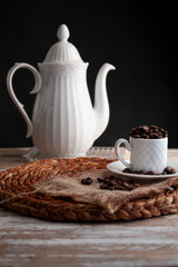 classic white espresso mug with coffee beans inside and a teapot in a black rustic background