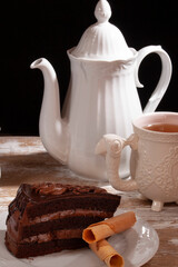 chocolate cake in a rustic scene concept with a classic white mug and teapot on a wooden table in a black background
