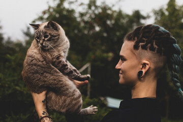 A beautiful young girl of unusual appearance on the street in the summer holds a cat in her arms.