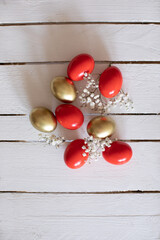 Red and gold Easter eggs decorative arranged with  tine flowers on white wooden table.