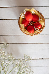 Red Easter eggs decorative arranged in basket and whit tine flowers on wooden table.