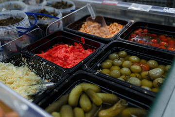 Soft focused shot of vegetable department in grocery store, supermarket, mall, hypermarket or shopping center. Boxes with pickled green and red tomatoes, cabbage, ginger, shrimps and cucumbers.