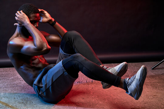 shirtless muscular black man pump the press on the floor alone, red neon light on his muscular body