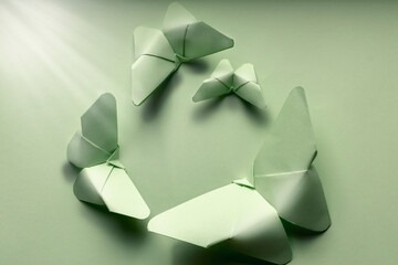 Obraz premium Butterflies of various sizes of green color from paper in origami art on isolated green background illuminated by a ray of light.