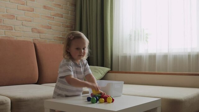 Little girl playing wooden figures on the table. Put the cubes in a box. Medium Shot.