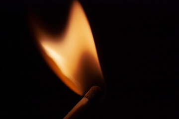 Horizontal close-up conceptual photography of a single wooden burning with bright orange hot flame match on the darkness