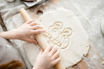 View from above. Girl rolls out dough for cookies on a wooden board with her hands in flour. Family...