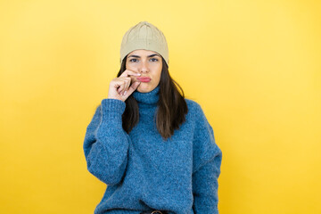 Young beautiful woman wearing blue casual sweater and wool hat mouth and lips shut as zip with fingers. Secret and silent, taboo talking