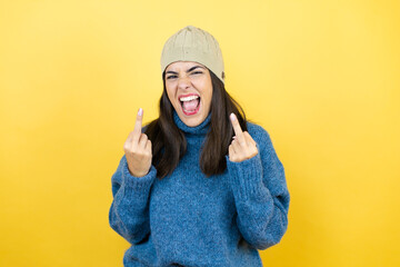 Young beautiful woman wearing blue casual sweater and wool hat showing middle finger doing fuck you bad expression, provocation and rude attitude. screaming excited