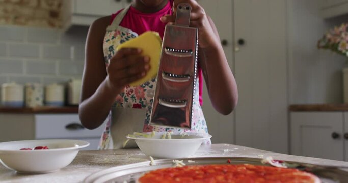 African american girl making pizza grating cheese in kitchen