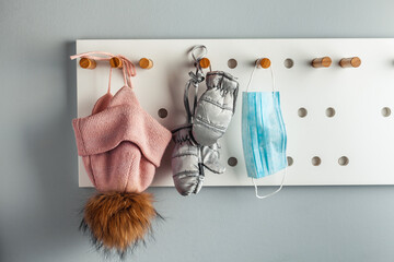 Pink mask for a girl hanging on a stylish hanger next to the children hat and gloves. Healthcare during Coronavirus quarantine. Prevent COVID-19