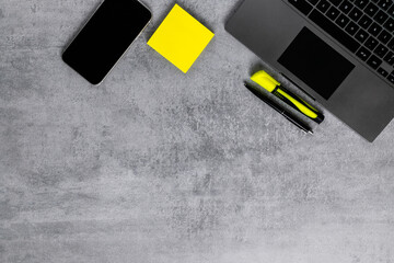 Laptop, phone, and office supplies on a gray concrete table. Workplace. A study table. Remote work. Distance learning. uminous yellow and extremely gray. The color of 2021. Copy space