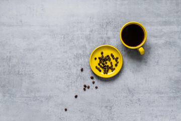 Coffee in a yellow cup. Coffee beans scattered on a gray concrete table