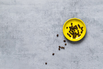 Coffee beans on a yellow plate, scattered grains on a gray concrete table