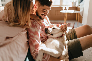 Dog lies on legs of owner. Man in pink shirt and his beloved woman admire their white pet