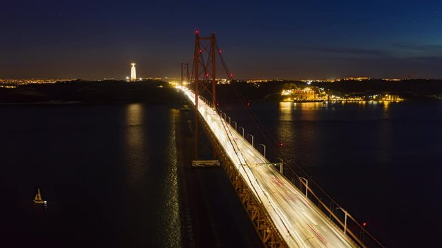 Drone flying over Ponte 25 de Abril at night, Lisbon, Portugal, Europe. Aerial view of cars driving on bridge in night time. Suspension bridge over Tagus river in Lisbon. 4k footage in hyperlapse