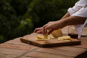 Man picking cheese of a wooden cheesboard on a terrace surrounded by trees