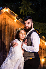 Newlywed couple, bride and groom on the background of an old wooden house and retro garland. Rustic winter wedding.