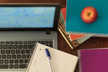 Top view of computer, books, notebook, pen and apple. Online homeschooling