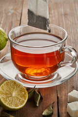 Tea in a transparent cup next to a tea bag, lime and sugar on a wooden background