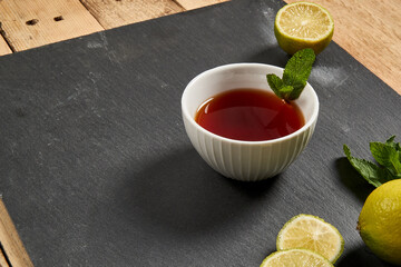 Tea in a white mug stands on a stone panel next to marshmallows and lime. There are pieces of spice for tea