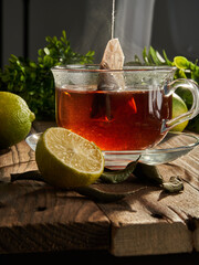 Tea in a tea bag is brewed in a transparent mug next to lime and sugar. Close-up