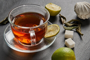 Tea in a white mug stands on a stone panel next to marshmallows and lime. There are pieces of spice for tea