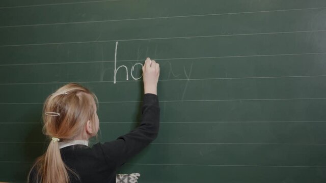 A girl of primary school age writes an inscription on the blackboard - a holiday.
