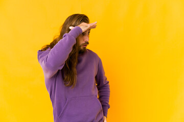 Young man with long hair look looking far away keeping hand on forehead.