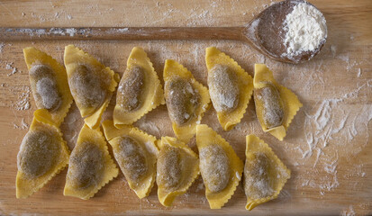 Freshly made Italian pasta ( mushroom filled triangle ravioli) on a wooden table. Wooden spoon with flour. Close up.