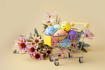Easter composition with colorful eggs in shopping cart and spring flowers on pastel background. Copy space.