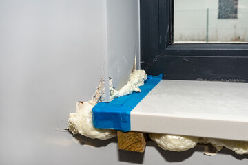 Newly installed white conglomerate window sill inside the room. Propped on a peg and filled with mounting foam from the bottom.