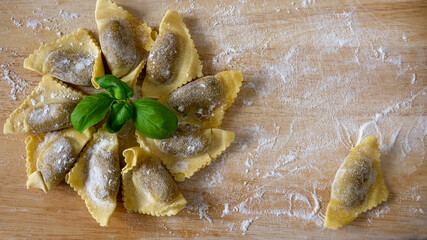 Authentic freshly made Italian pasta (mushroom filled triangle ravioli) -group and one piece separate on a wooden cutting board sprinkled with flour. Close up.