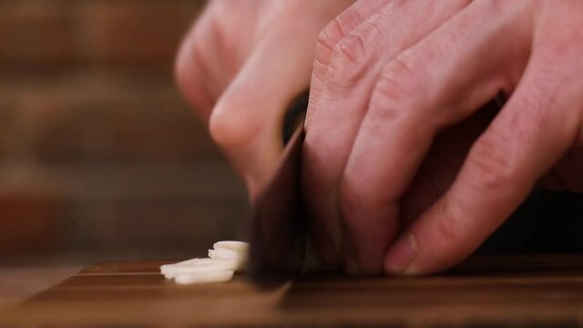 Chef slicing garlic cloves on a wooden board.