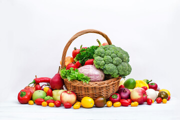 Assorted organic vegetables and fruits in wicker basket isolated on white background.