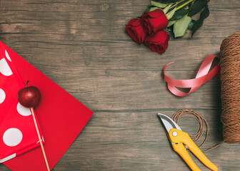 Florist workplace Top view photo with copy space Red rose flowers, gardening scissors, bright red wrapping paper and different ribbons on wooden table