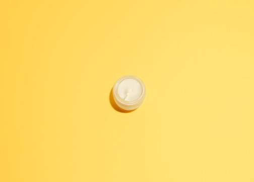 Skincare cream Top view photo in minimal style with copy space Opened glass jar with white smooth cream on yellow background