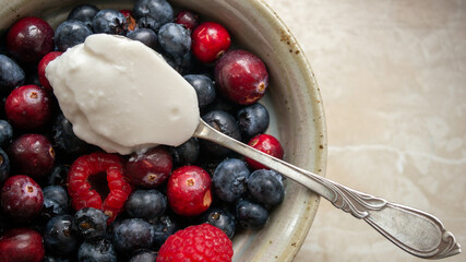 Wild organic berry bowl with vegan coconut yogurt on a silver vintage spoon for breakfast. Clean eating. Close up.