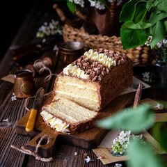 homemade rectangular layered sponge cake decorated with white and chocolate cream on rustic table with bouquet of lilac