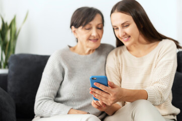 An adult daughter explains to senior mother how to send messages on the smartphone, help to...