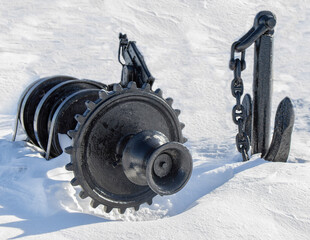 Black steel anchor, anchor chain and anchor windlass partly buried in snow nobody