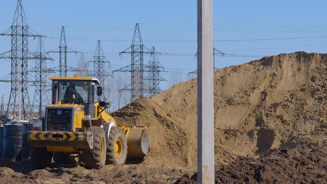 Wheel loader, with its large bucket in front, moves large amounts of land and creates large mountain at the construction site 