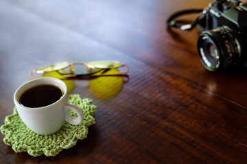 Xícara com café, câmera antiga e óculos com lentes amarelas sobre uma mesa de madeira.